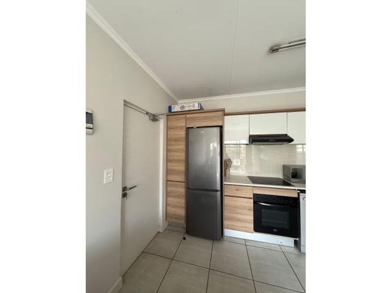 A compact kitchen featuring wood-grain cabinetry, a built-in oven, extractor fan, and tiled flooring, providing a functional and modern cooking space.