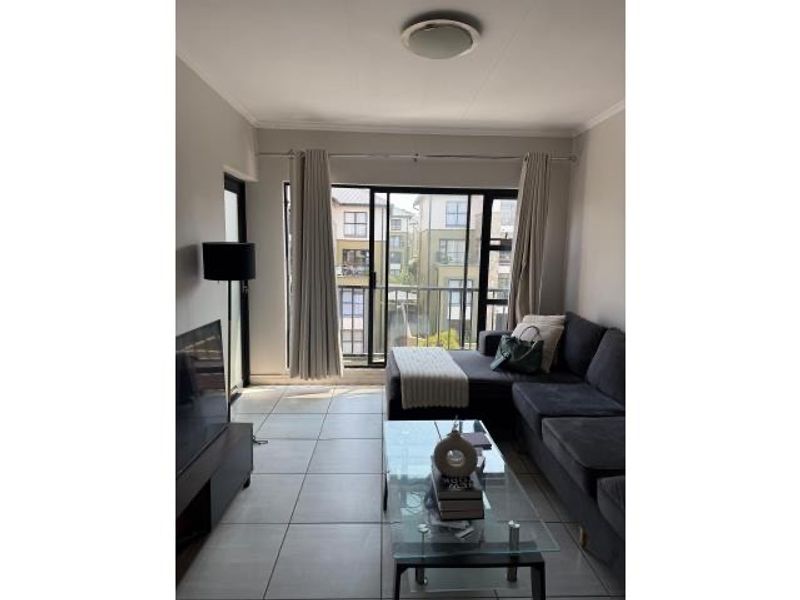A bright living room featuring large sliding glass doors that open onto a balcony, with neutral tiled flooring throughout.