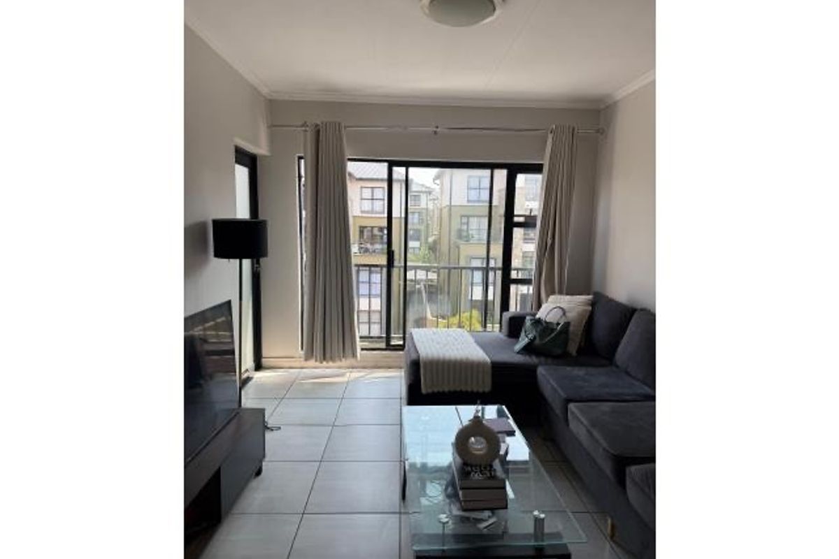 A bright living room featuring large sliding glass doors that open onto a balcony, with neutral tiled flooring throughout.