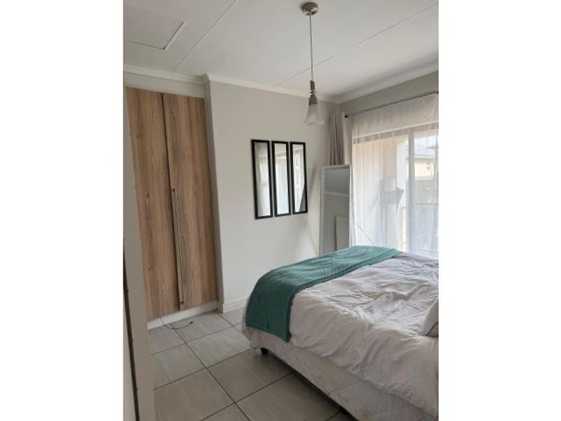 A well-maintained bedroom featuring built-in wooden cabinetry, tiled flooring, and a sliding door providing access to a balcony.