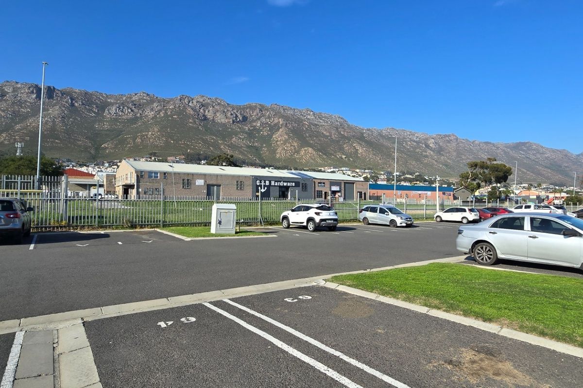 A wide-angle view of a paved parking area with mountain views in the background, featuring perimeter fencing and landscaped grass verges.