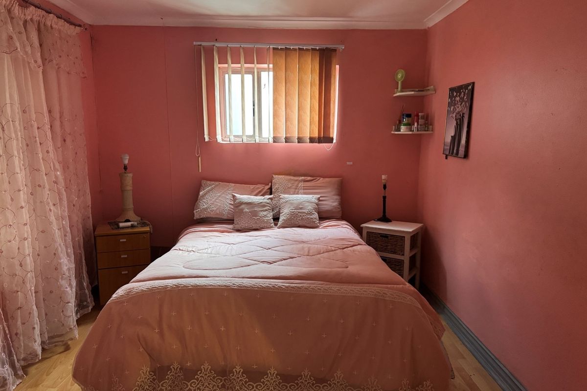 A bedroom featuring pink walls, a window with security bars, and built-in wall shelving, offering a blank canvas for potential cosmetic updates.