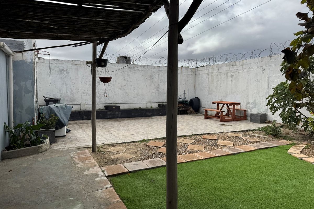 A rear courtyard featuring a tiled patio area, timber pergola, and perimeter wall with security fencing, offering a private outdoor space.