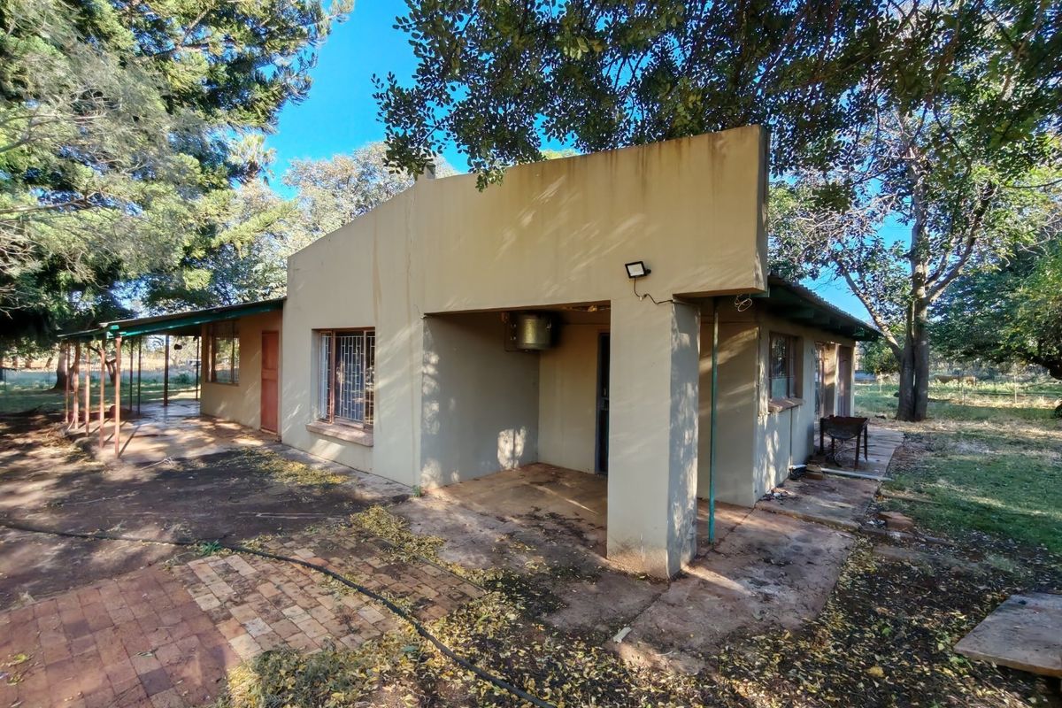 Exterior view of a farm dwelling featuring a covered patio area, brick paving, and mature surrounding trees.