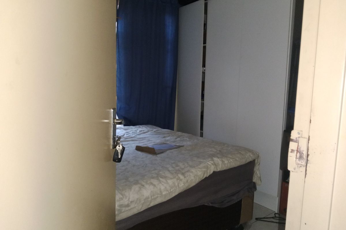 A bedroom featuring built-in wardrobe cabinetry and tiled flooring, viewed through a partially open doorway.