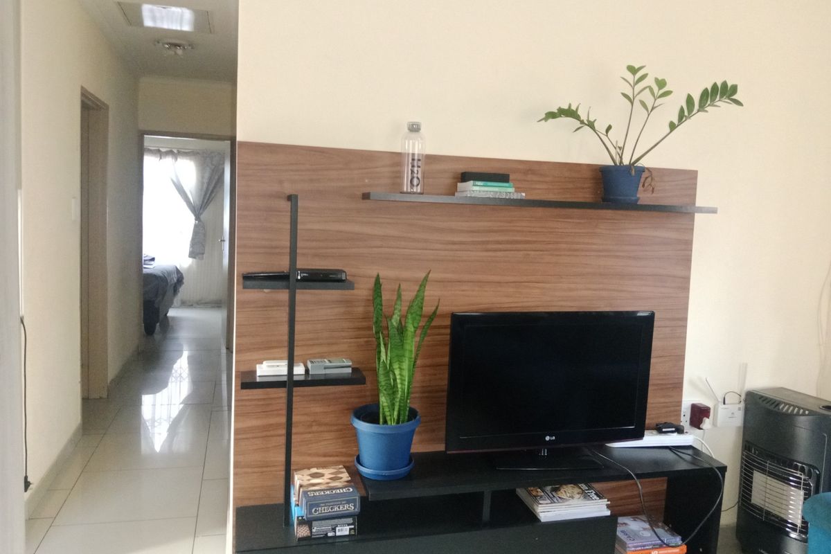 A living area featuring a wood-look feature wall panel with integrated shelving and tiled flooring, leading into a hallway.