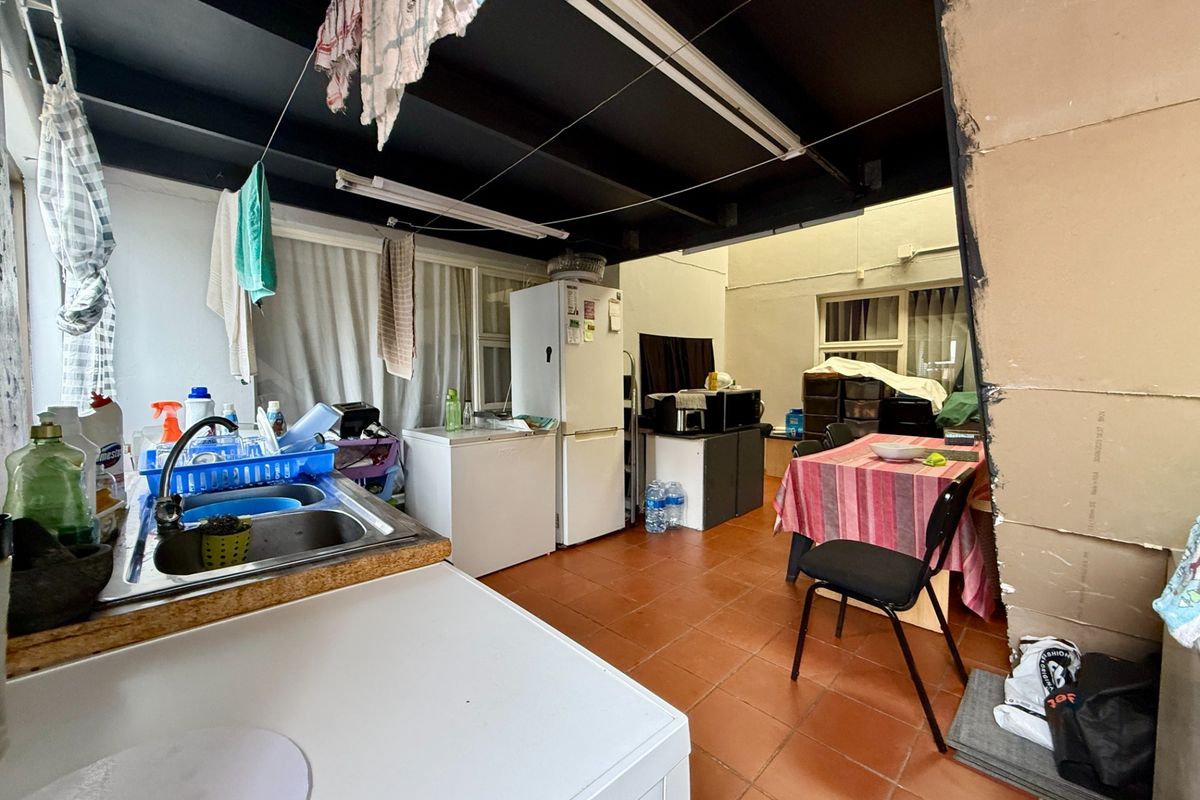 A functional kitchen and dining area featuring tiled flooring, a stainless steel sink, and an exposed ceiling structure.
