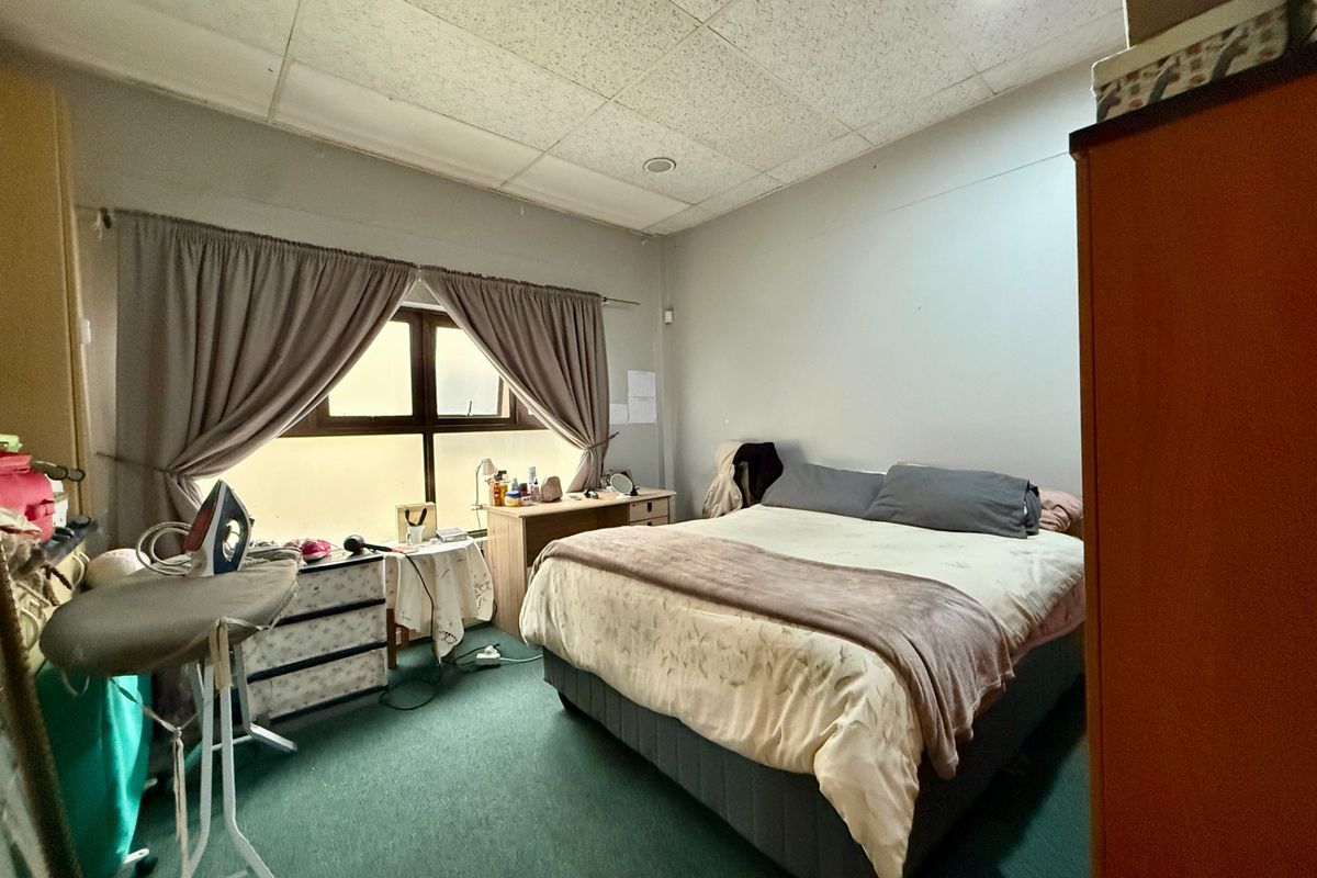 A bedroom featuring a drop ceiling, carpeted flooring, and a window with curtains, providing a functional sleeping space.