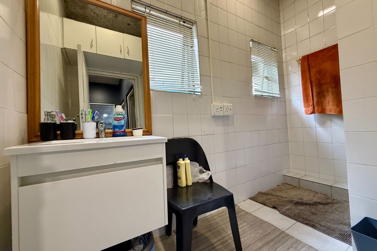 A functional bathroom featuring a wall-mounted vanity with mirror, tiled walls, and a dedicated shower area with a raised step.
