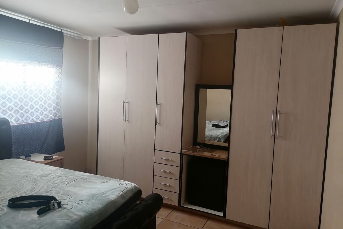 A bedroom featuring built-in light wood-toned cabinetry with integrated drawers and a vanity mirror section, complemented by tiled flooring.