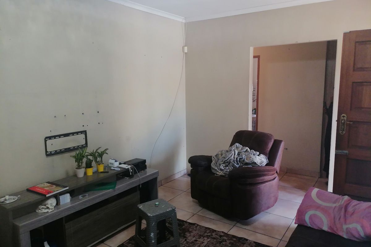 A living room area featuring tiled flooring, a wall-mounted television bracket, and a doorway leading to an adjacent space.