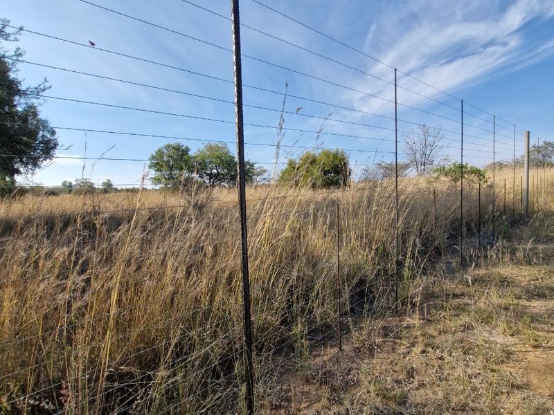 A view of the farm perimeter featuring standard wire fencing with metal posts, set against a backdrop of dry grassland and open sky.