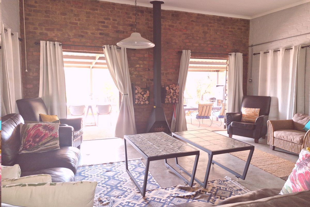 Spacious living room featuring an exposed brick feature wall, a central wood-burning fireplace, and large glass doors opening onto a covered patio.
