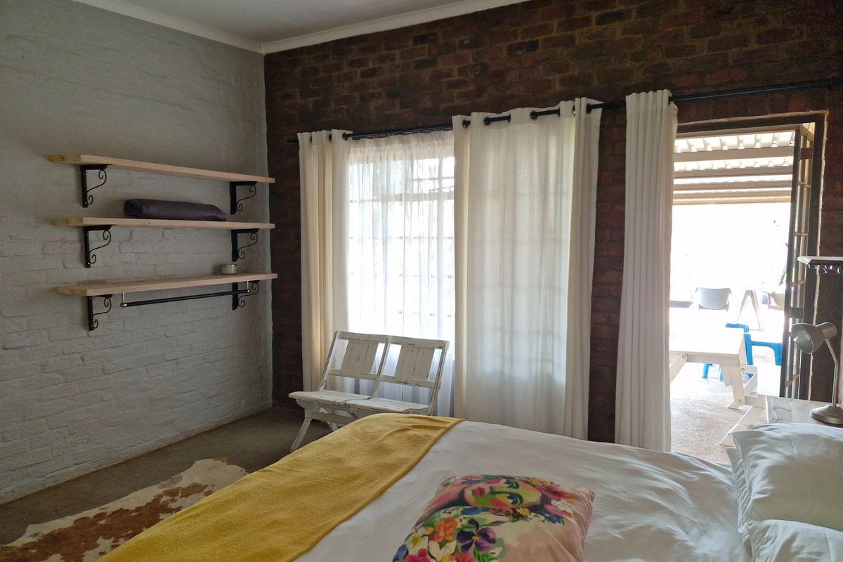 A bedroom featuring exposed brick walls, built-in wooden shelving, and direct access to an outdoor patio area.