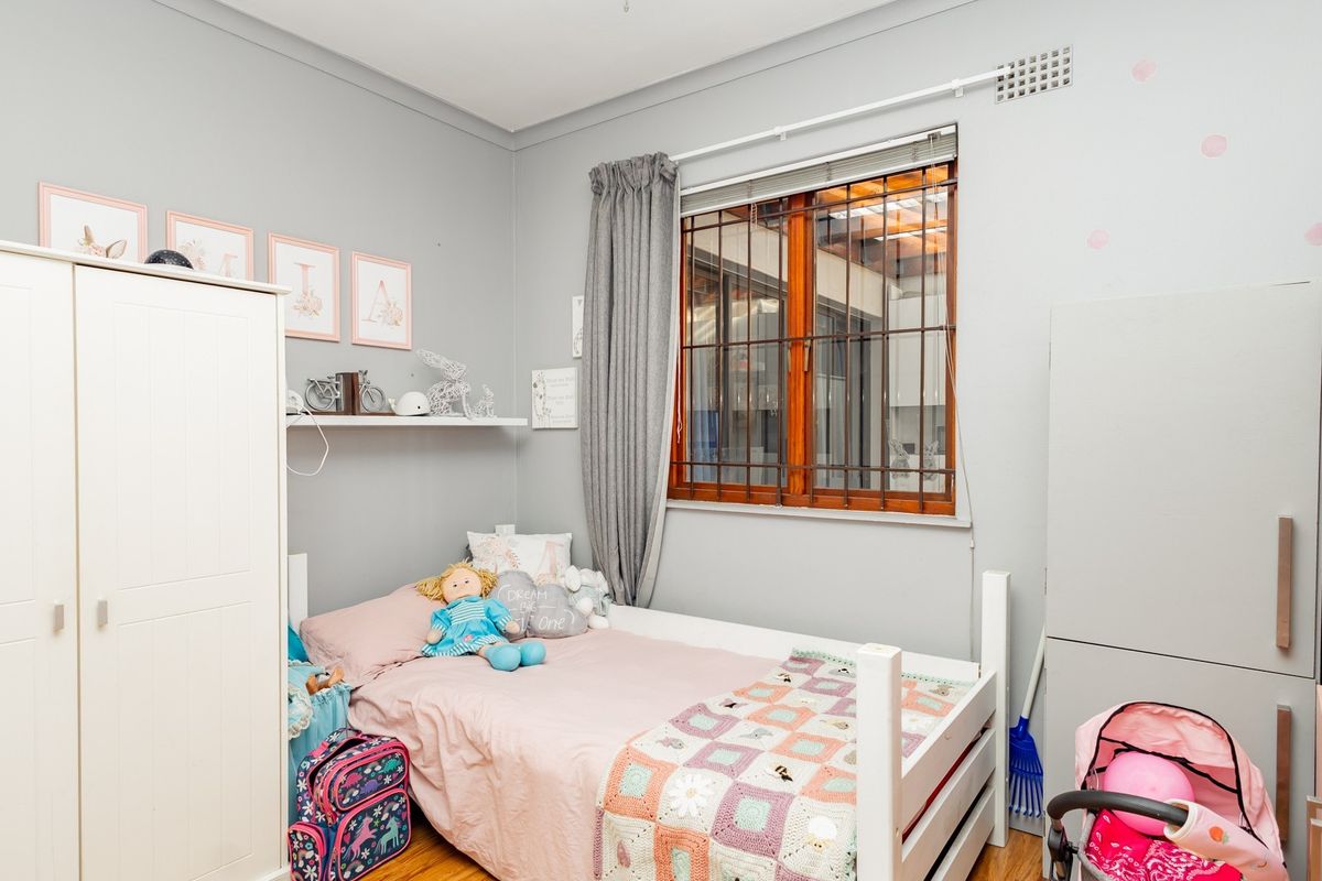 A bedroom featuring timber flooring, a window with security bars, and built-in cabinetry.