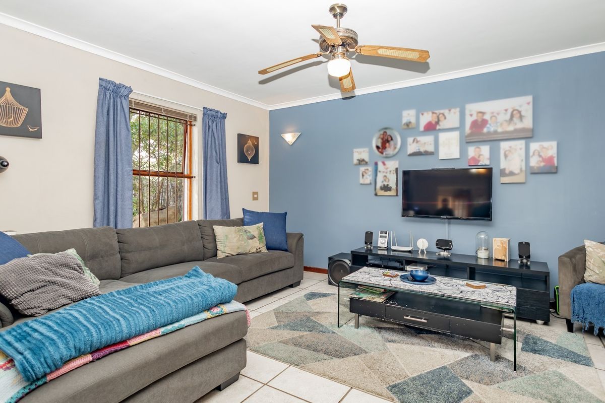 A comfortable living room featuring tiled flooring, a ceiling fan, and a blue accent wall, providing a functional space for relaxation.