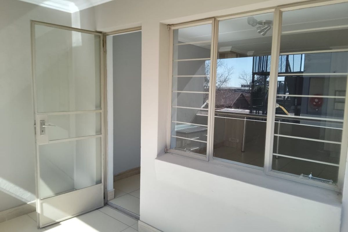 A bright, tiled interior space featuring large windows with security bars and a glass-panelled door leading to an adjacent room.