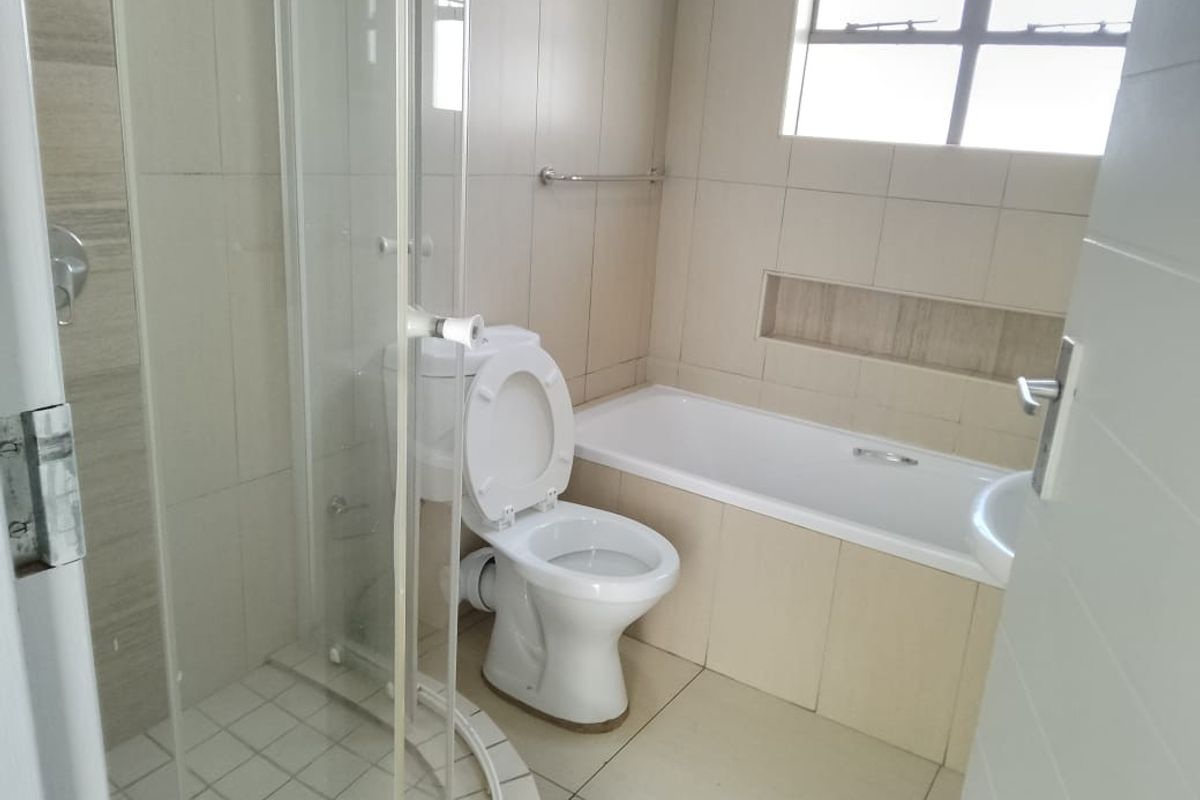 A functional bathroom featuring a glass-enclosed shower, a built-in bathtub, a toilet, and tiled walls with a recessed shelf.