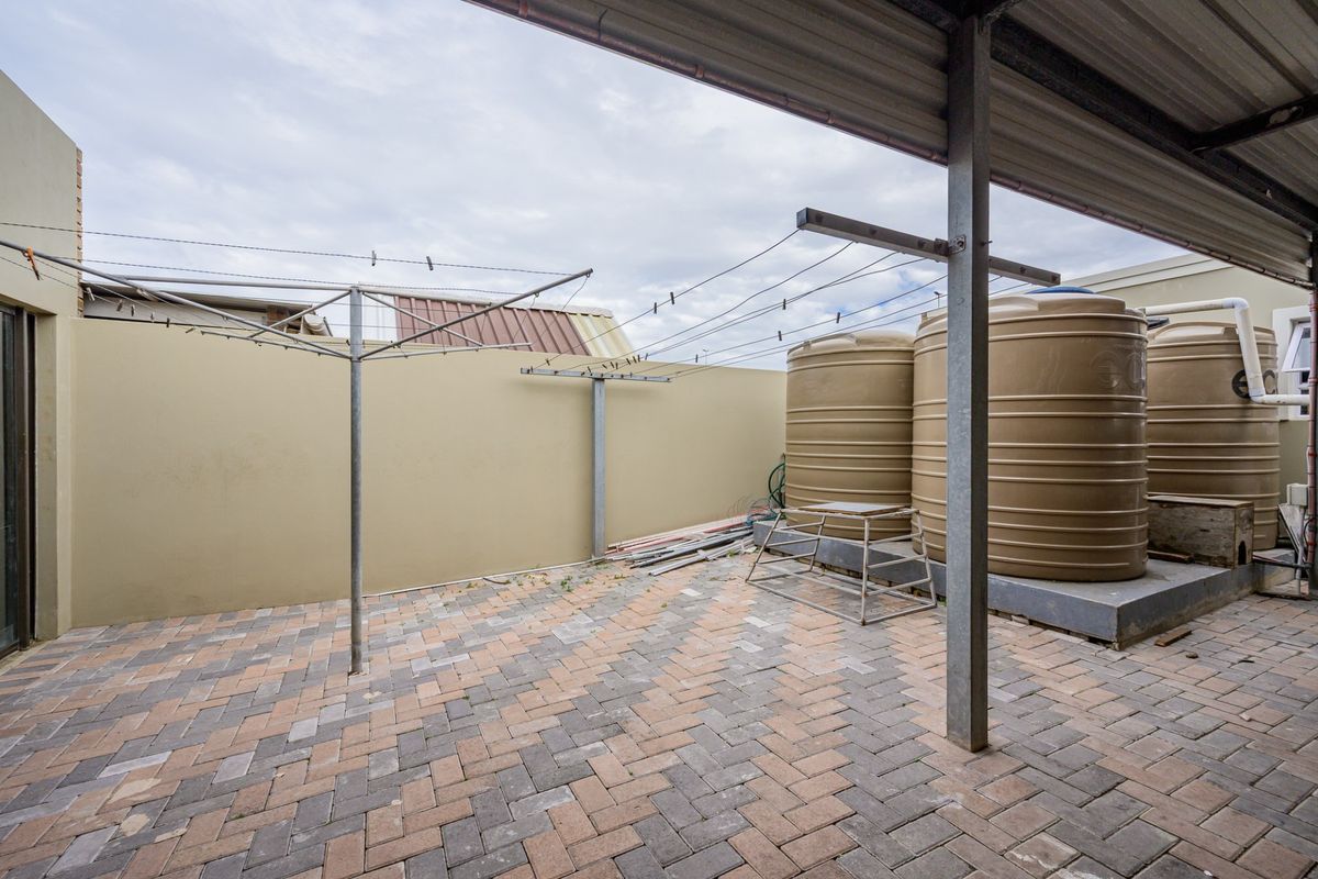 A paved rear courtyard featuring a covered patio area, multiple water storage tanks, and a rotary clothesline against a boundary wall.