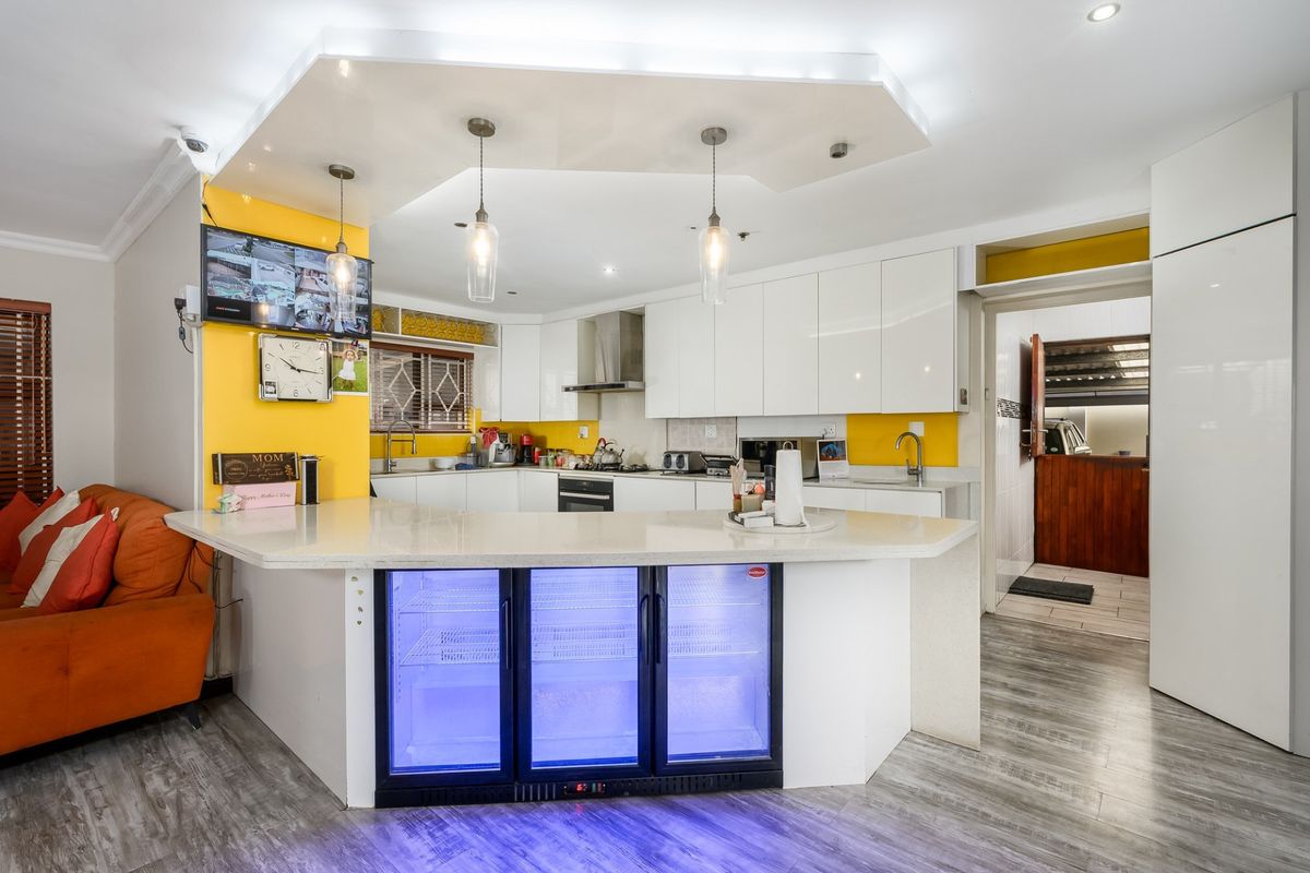 Modern kitchen featuring white high-gloss cabinetry, stone countertops, integrated beverage cooler, and a stylish drop ceiling with recessed and pendant lighting.