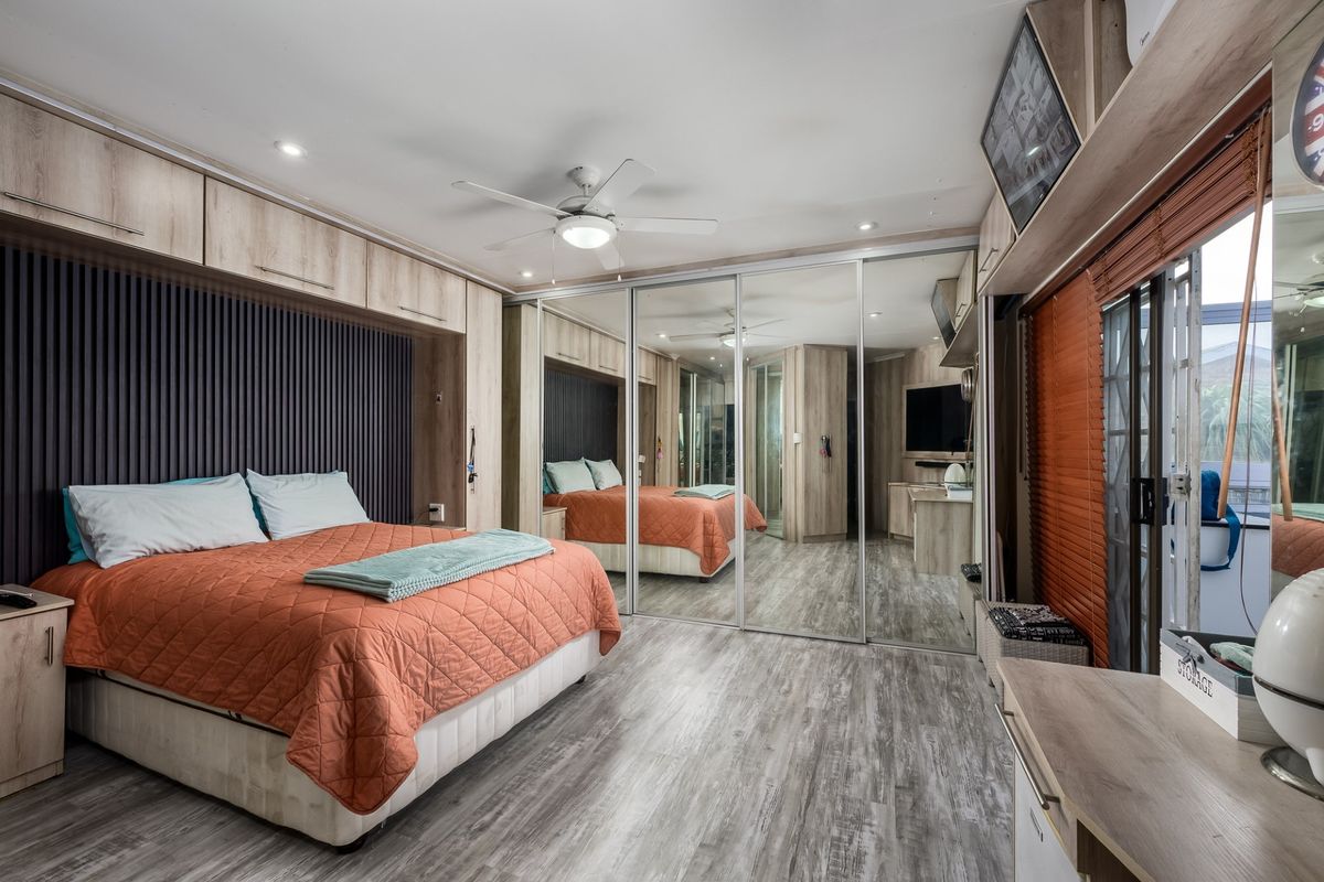 A well-appointed bedroom featuring extensive built-in cabinetry, mirrored wardrobe doors, modern slatted wall detailing, and a ceiling fan with integrated lighting.