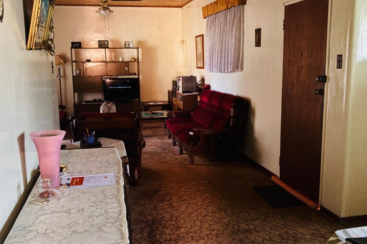 A living room featuring a timber-paneled ceiling, ceiling fan, and carpeted flooring, offering a dated aesthetic ready for modernization.