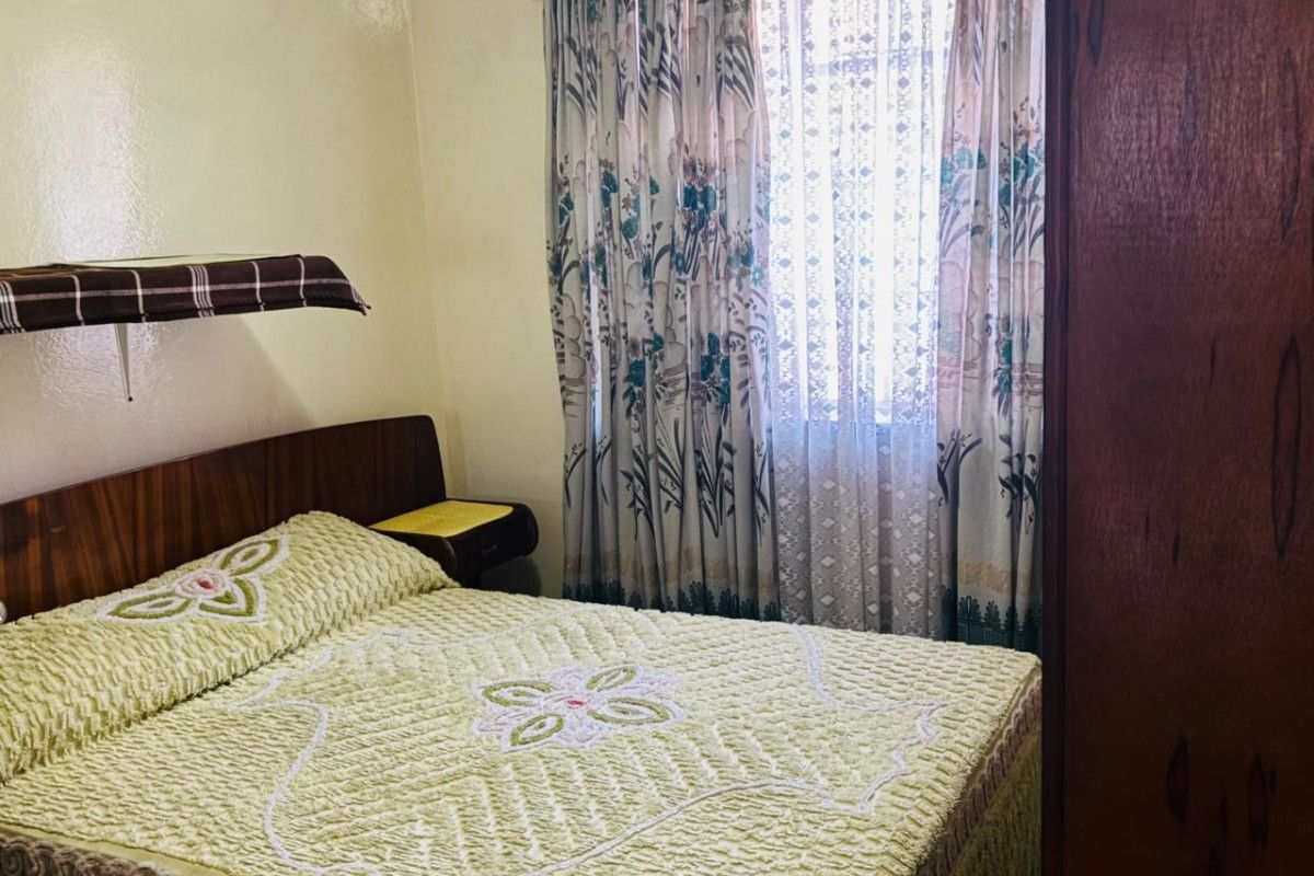 A bedroom featuring a built-in headboard and window with curtain rails, offering a functional space ready for modern updates.