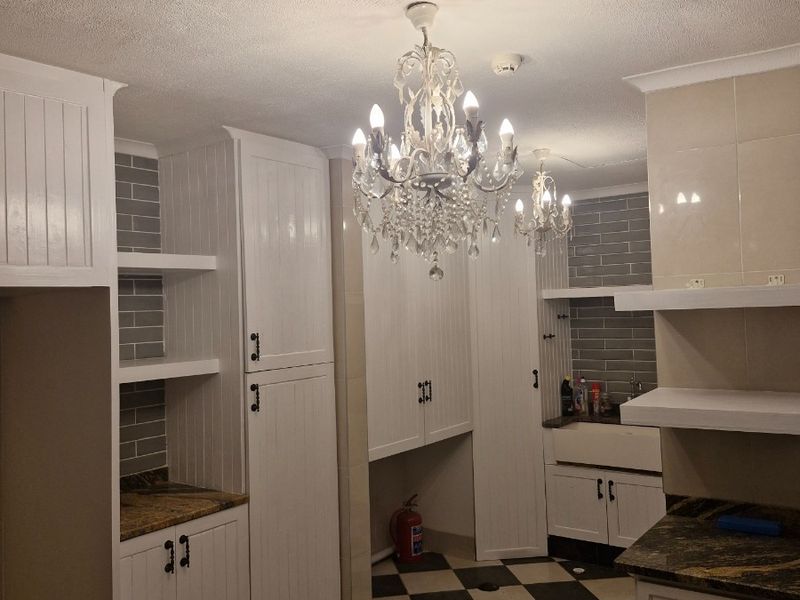 A spacious scullery featuring white built-in cabinetry, granite countertops, a farmhouse sink, and classic checkerboard floor tiles.