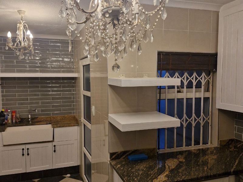 Kitchen featuring farmhouse sink, granite countertops, tiled backsplash, and built-in cabinetry with a decorative chandelier.