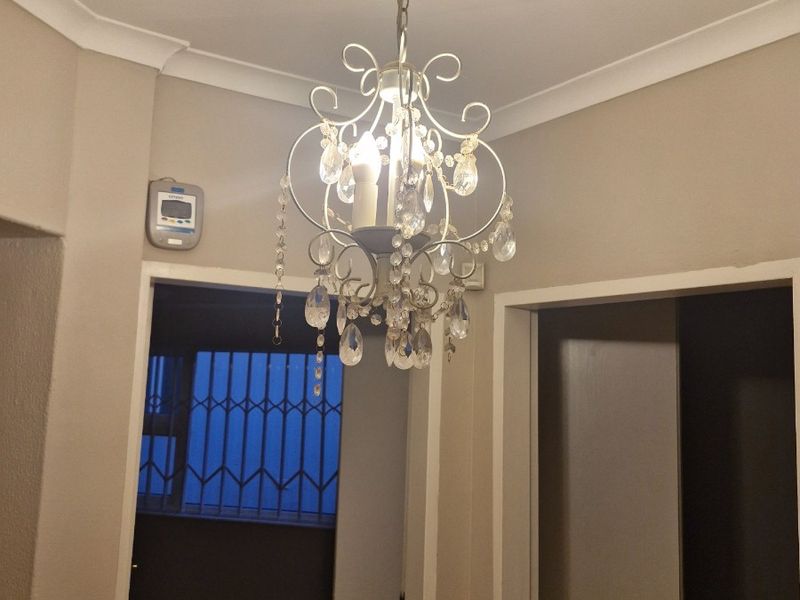 A well-lit hallway featuring decorative coving and a classic crystal chandelier, providing access to adjacent rooms.