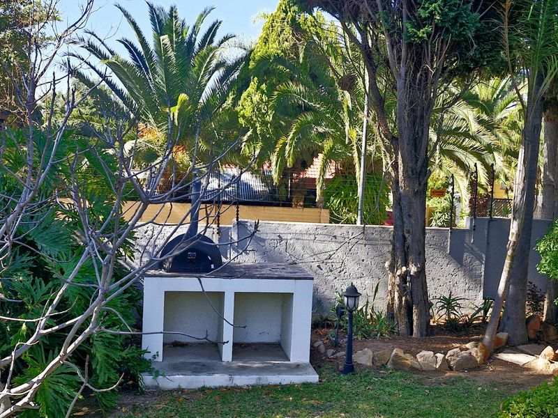 A private garden area featuring a built-in masonry braai or barbecue station, established trees, and a secure perimeter wall.