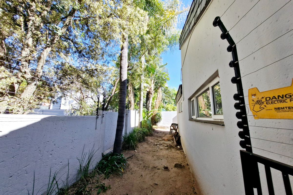 A narrow side passage of the townhouse featuring a perimeter wall with an electric fence and mature trees.