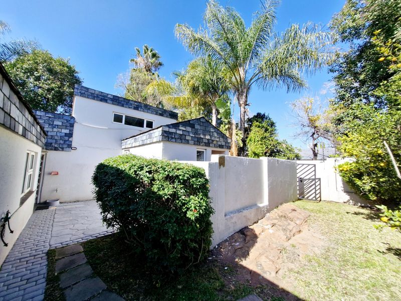 A rear exterior view of the townhouse featuring a paved patio area, white rendered walls, slate roof detailing, and a private garden space.