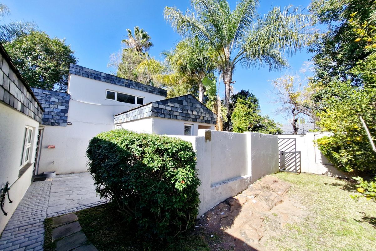 A rear exterior view of the townhouse featuring a paved patio area, white rendered walls, slate roof detailing, and a private garden space.