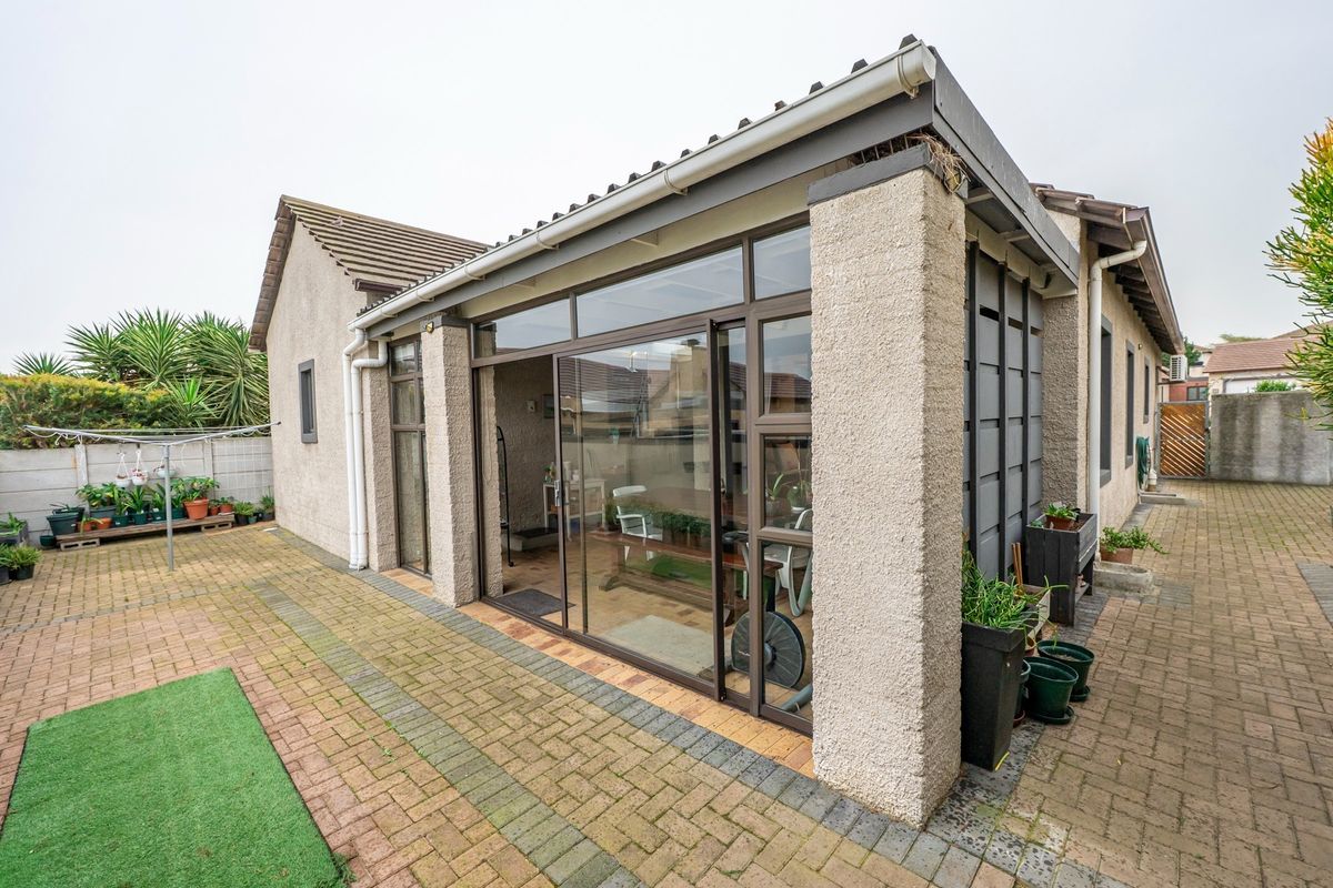 Rear view of the property featuring a paved courtyard, covered patio area with large sliding glass doors, and low-maintenance exterior finishes.