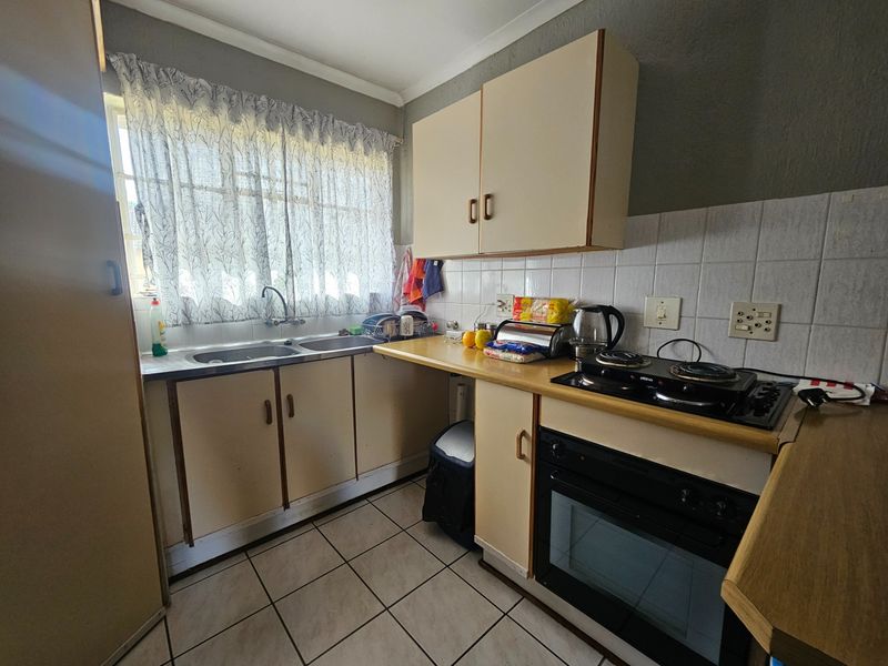 A compact, dated kitchen featuring laminate cabinetry, a built-in oven with hob, double sink, and tiled flooring.