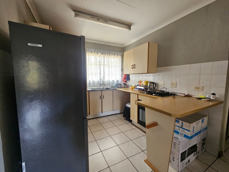 A compact kitchen featuring tiled flooring, built-in cabinetry, a sink, and a small breakfast counter, offering a functional layout in need of modernization.