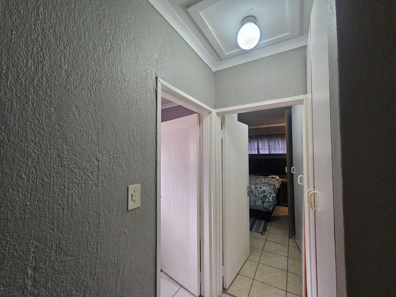 A functional hallway featuring tiled flooring, built-in storage cupboards, and access to adjacent bedrooms.