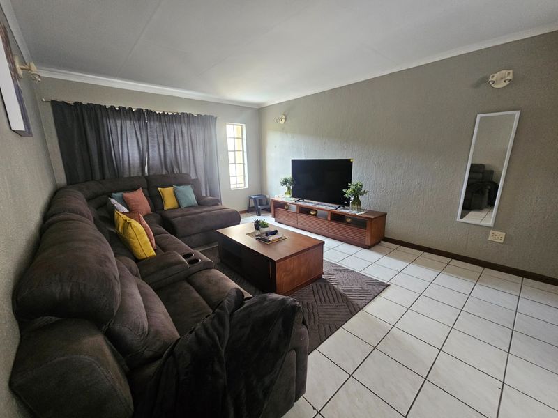A spacious living room featuring tiled flooring, neutral wall finishes, and large windows, providing a comfortable and functional area for relaxation.