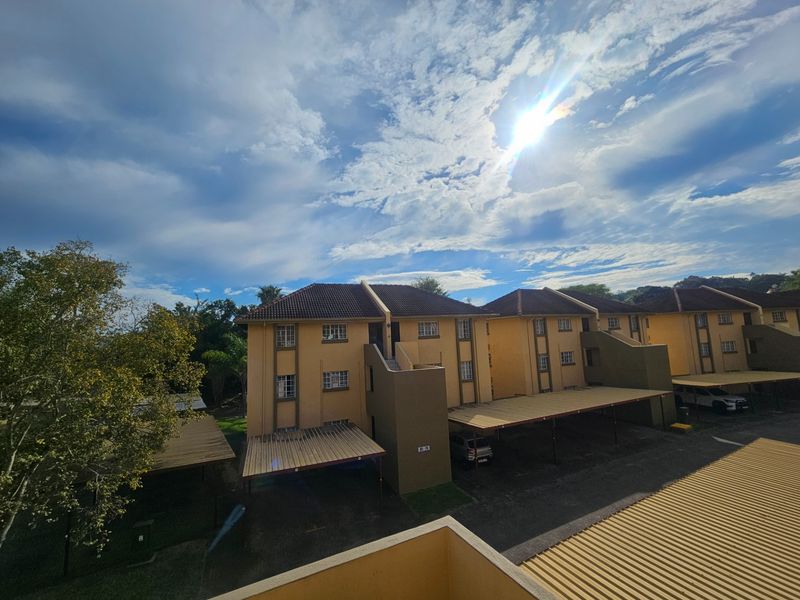 An elevated view of an apartment complex featuring yellow facades, tiled roofs, and covered parking bays for residents.