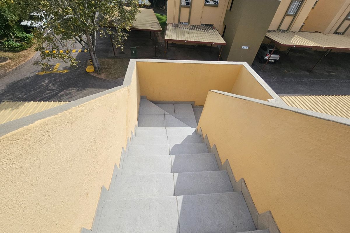 An elevated view looking down an external staircase with tiled steps and painted masonry walls, overlooking the apartment complex parking area.