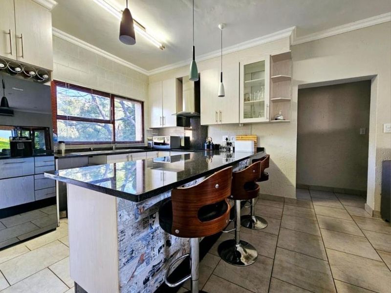Modern kitchen featuring granite countertops, ample built-in cabinetry, a breakfast bar, and ceramic floor tiles, offering a functional and well-lit cooking space.
