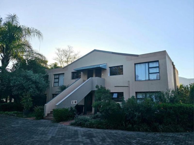Front elevation of a two-story apartment building featuring a paved driveway, external staircase, and established garden landscaping.