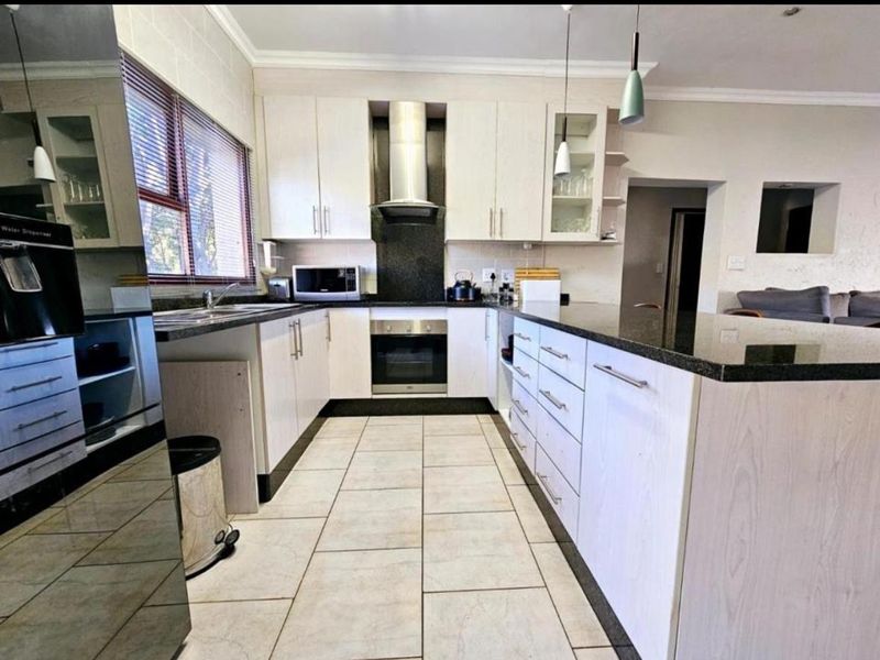 Modern kitchen featuring light wood cabinetry, dark granite countertops, built-in oven, stainless steel extractor fan, and tiled flooring.