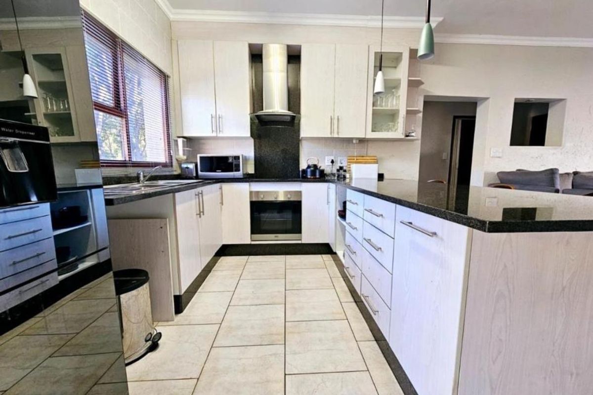 Modern kitchen featuring light wood cabinetry, dark granite countertops, built-in oven, stainless steel extractor fan, and tiled flooring.