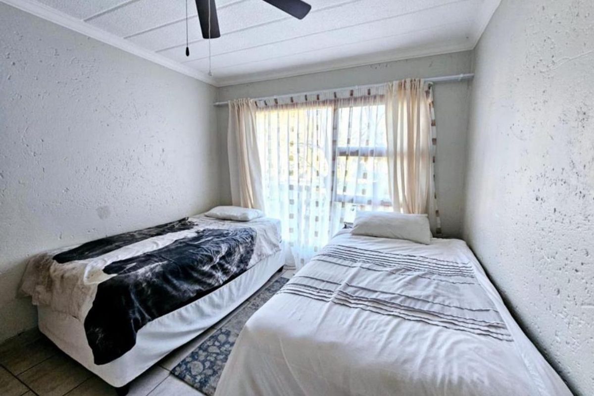 A compact bedroom featuring tiled flooring, a ceiling fan, and a sliding glass door providing natural light.