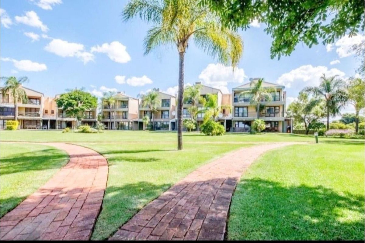 A view of the apartment complex exterior featuring well-maintained communal lawns, brick pathways, and mature palm trees under a clear blue sky.