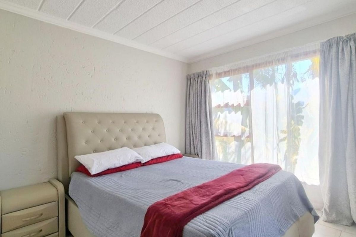 A bright bedroom featuring textured walls, a panelled ceiling, and large sliding glass doors that provide natural light and access to the outdoors.