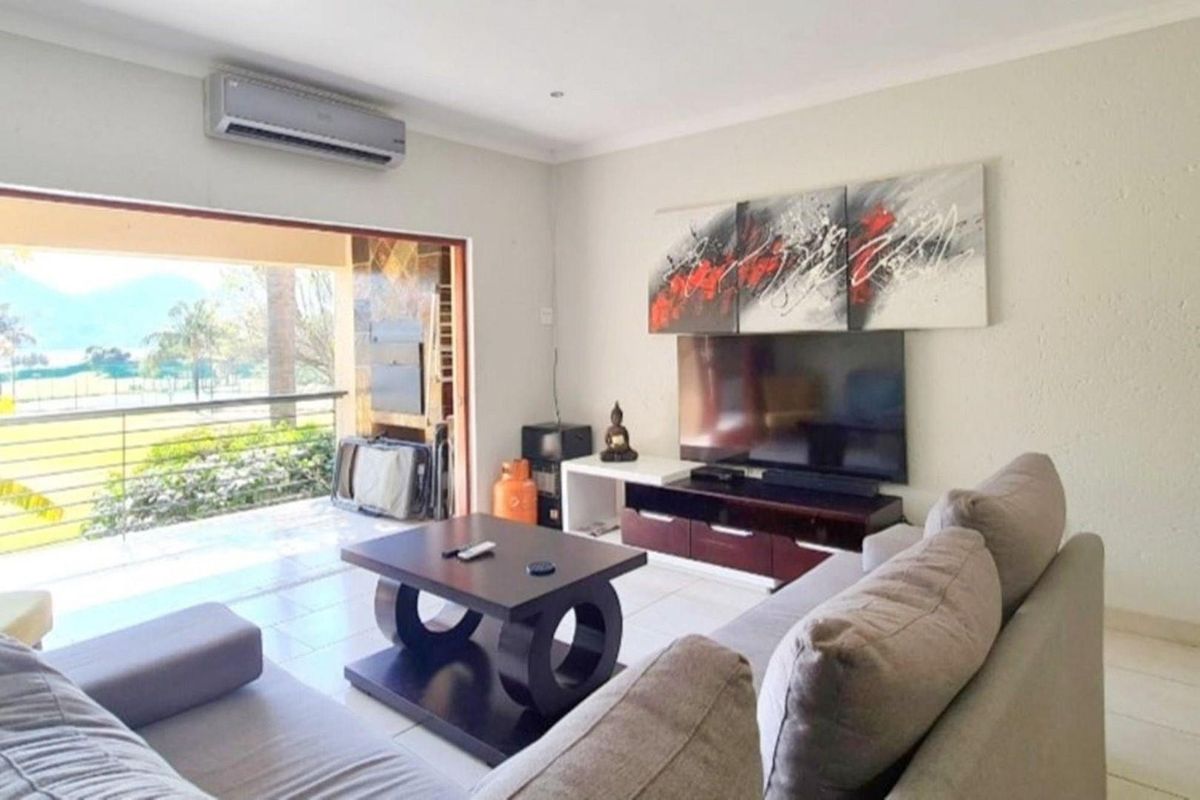 A bright living room featuring tiled flooring, a wall-mounted air conditioning unit, and large sliding doors opening onto a balcony with scenic views.