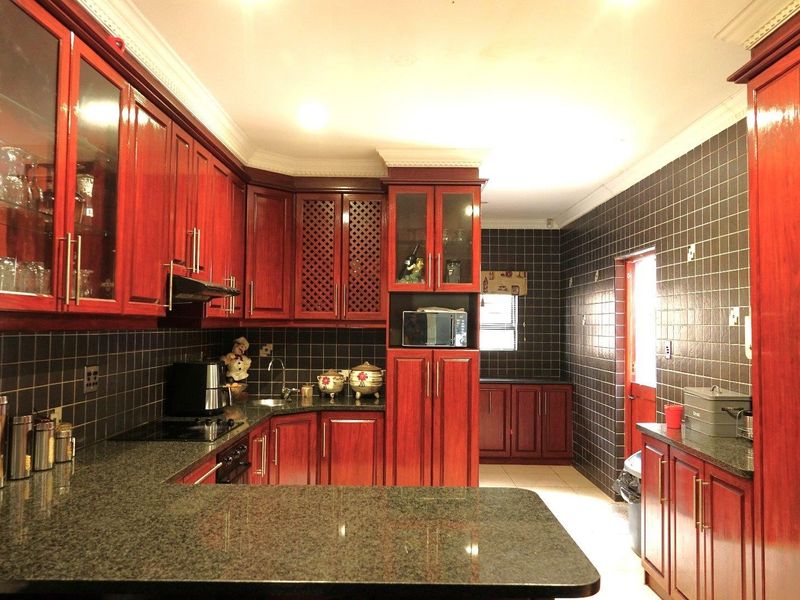 A spacious kitchen featuring dark wood cabinetry, granite countertops, and dark tiled walls, offering ample storage and workspace for culinary activities.